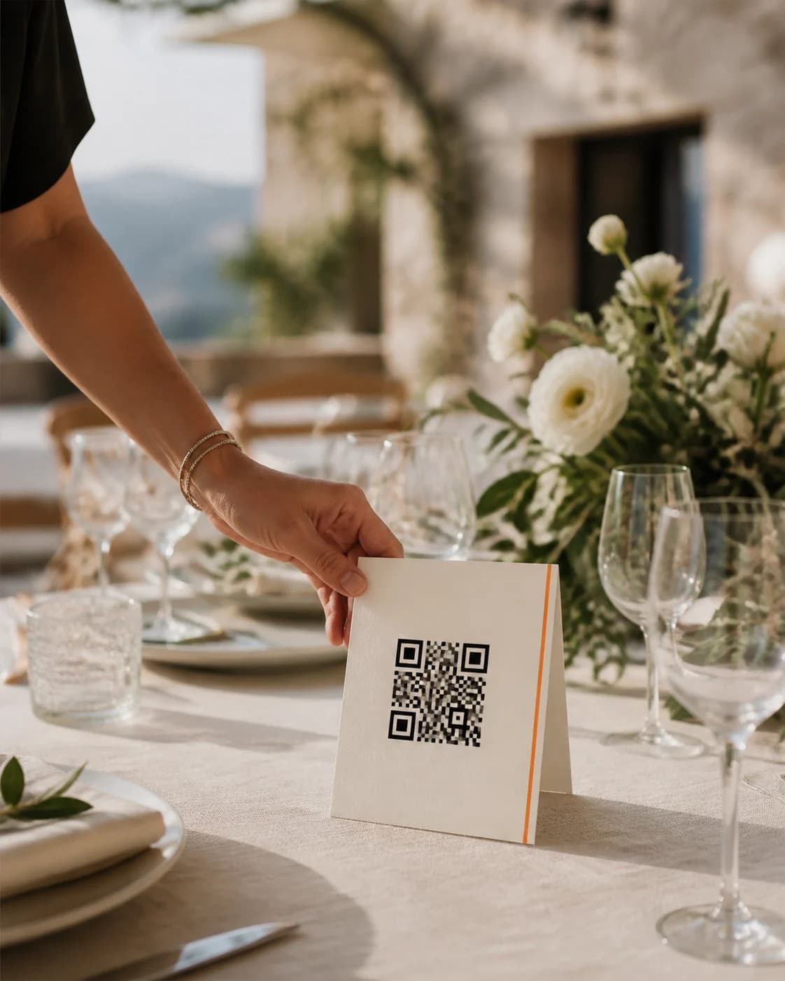 Düğün masasındaki çiçeklerin yanına QR kodlu albüm kartı yerleştiren bir el